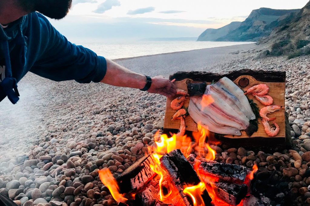 tim gibb of asado fire kitchen cooking fish and shellfish over a fire on the beach